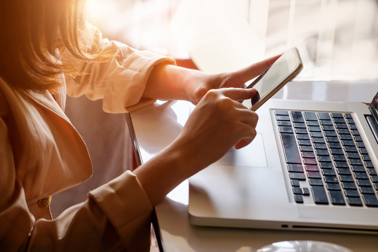 Closeup of woman's hands holding phone sitting in front of computer